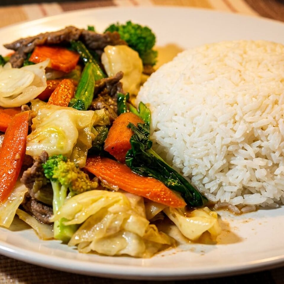 Beef stir-fry with mixed vegetables and white rice on a white plate.